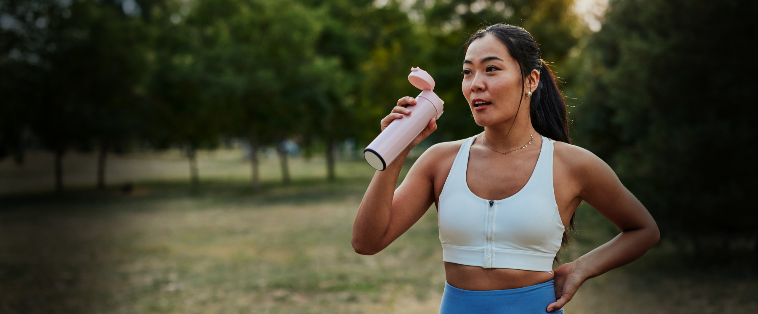 Person holding water bottle in park, dressed in workout gear.