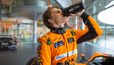 man in orange racing suit drinking from an optimum nutrition bottle