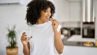 girl holding glass of water and taking supplement