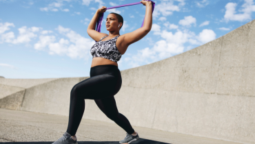 woman outside doing a lunge holding a fitness band above her head
