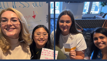 four women posing with whiteboard behind them and paper in their hands
