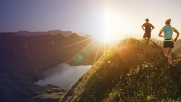 two people running on top of a mountain with a sun rise