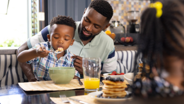 boy eating cereal in fathers lap
