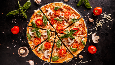 sliced up pizza surrounded by tomatoes and mushrooms