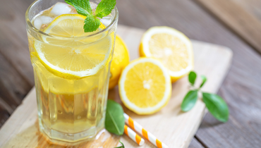 a glass with yellow liquid and a lemon in it beside halved lemons