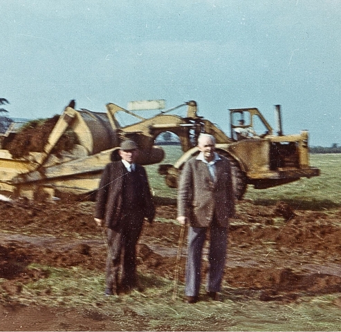 old picture of two men standing beside and excavator