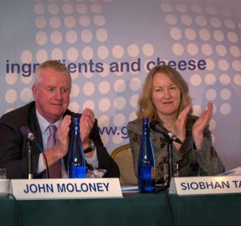 two people sitting at a table with microphones in front of them clapping
