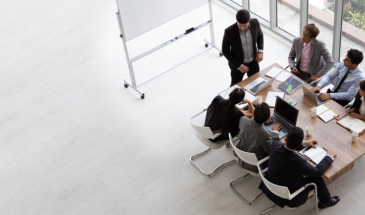 a group of people sitting around a table looking at a computer and presenter