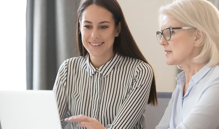 two woman looking at a laptop screen discussing work
