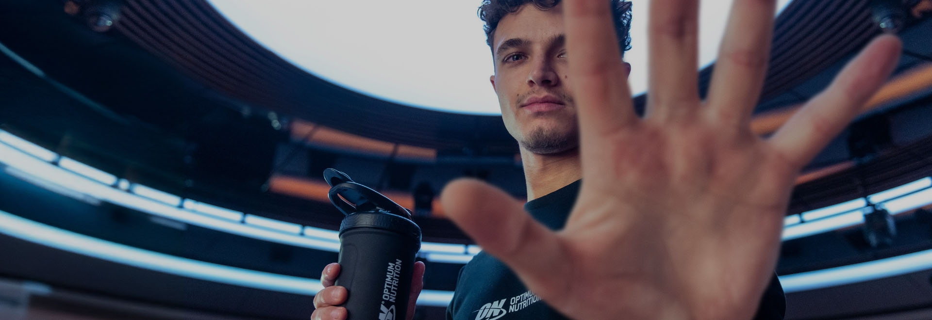 Person holding a black Optimum Nutrition shaker bottle with a hand partly covering their face.