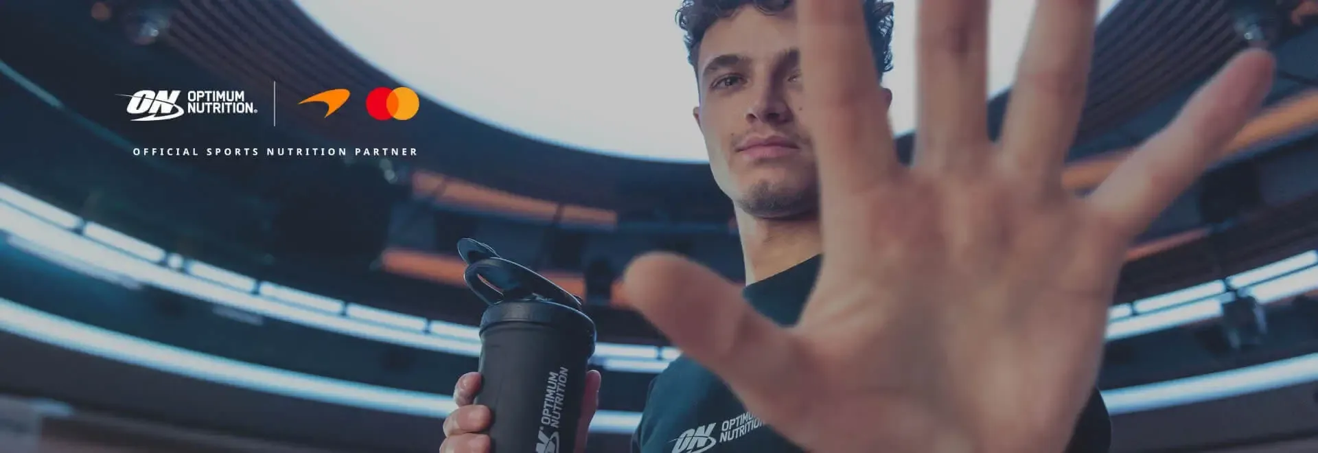 Person holding a black Optimum Nutrition shaker bottle with a hand partly covering their face.