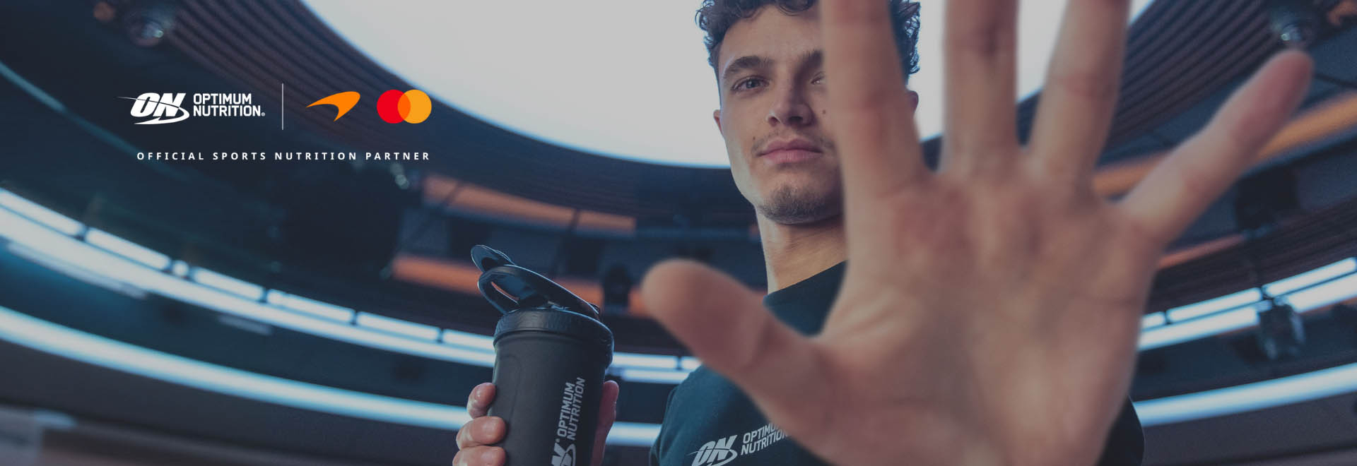 Person holding a black Optimum Nutrition shaker bottle with a hand partly covering their face.