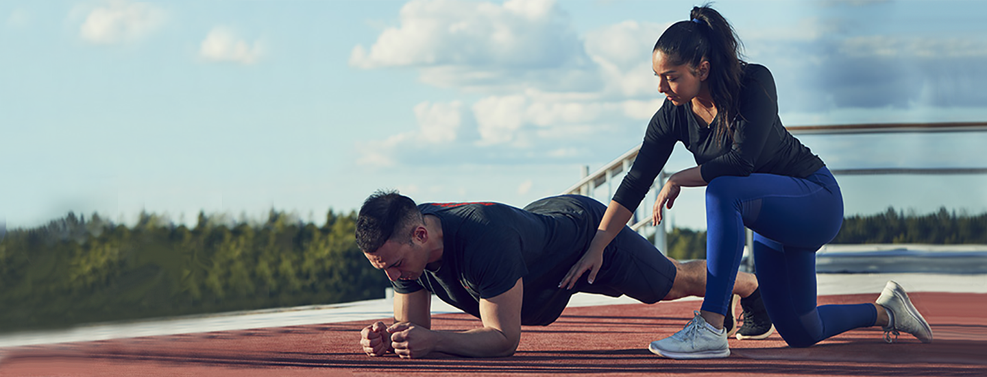 woman kneeling on one knee coaching a man planking on outside