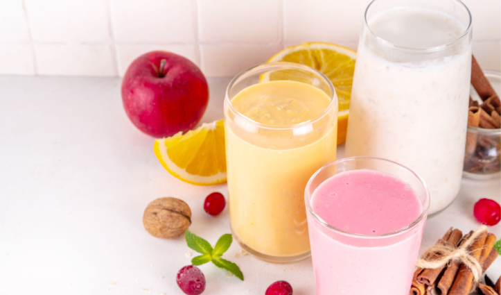 hree colorful smoothies in glasses surrounded by fruit slices, an apple, cranberries, nuts, and cinnamon sticks.
