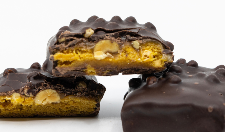 Chocolate‑coated bars with visible nuts and a golden cookie layer, shown in a close-up with one bar cut open.
