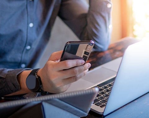a person using a mobile phone with laptop in front