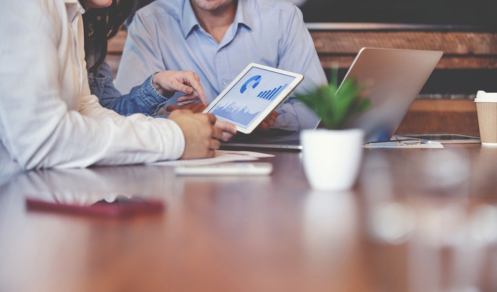 people sat around a table looking at a tablet with graphs on it