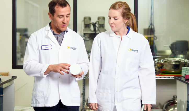 man and woman in white lab coats in a lab looking at a white container