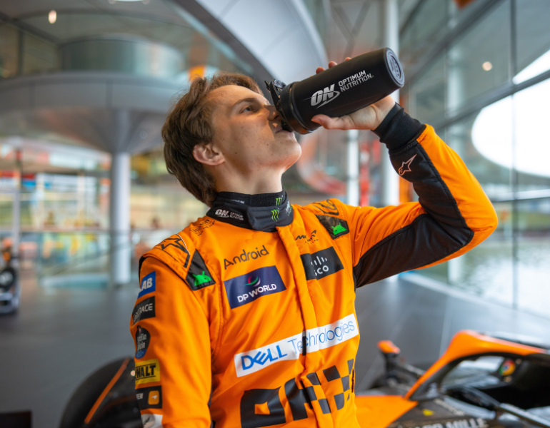 man in mclaren gear drinking out of an optimum nutrition bottle