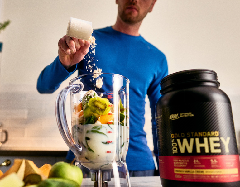 man pouring whey protein into a blender full of ingredients