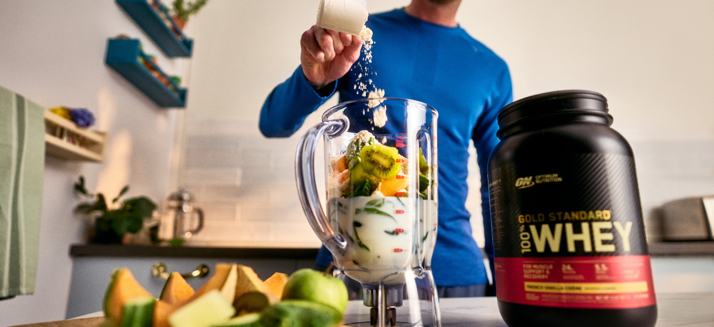 man putting protein powder and mixed fruit in a blender