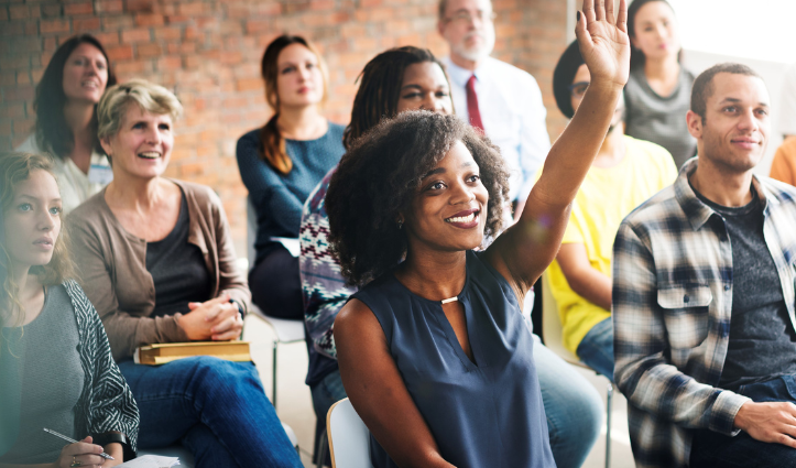 group of people listening to a speaker and one person with their hand raised