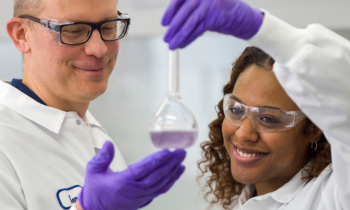 two people in lab coats with a purple liquid