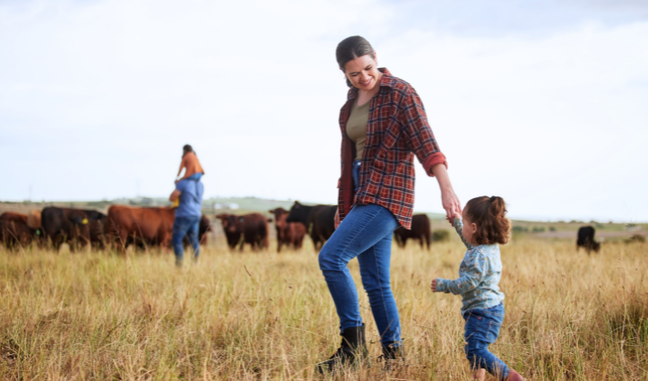 woman holding hands with child walking through field of cows