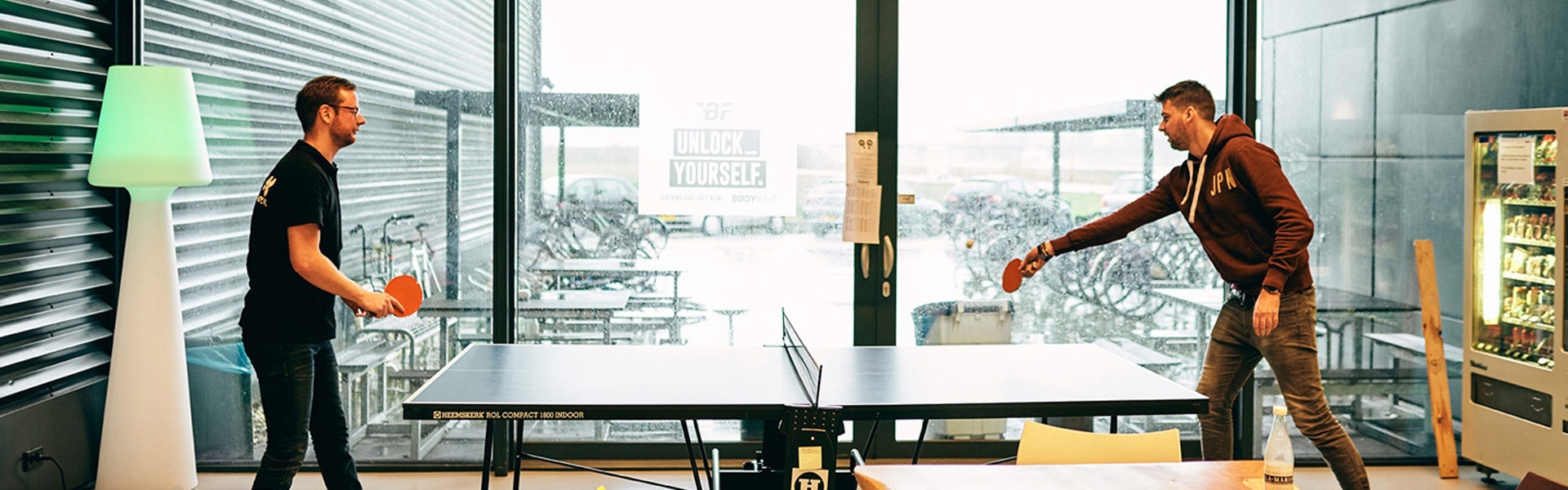 Two men playing ping pong with bats and a ping pong table