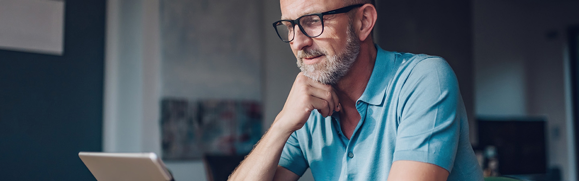 A man with glasses wearing a blue shirt looking at a tablet